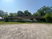 Front facade of 7348 Dupont Avenue at the time of auction — long single-story commercial building set in a clearing, low pitched roof, deferred maintenance visible.